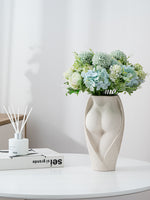 Modern ceramic flower vase with feminine silhouette, arranged with soft green and white blooms, enhancing elegant tabletop decor.