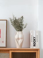 Modern ceramic flower vase with sculpted body design, styled with dried greenery on a wooden shelf for contemporary interiors.