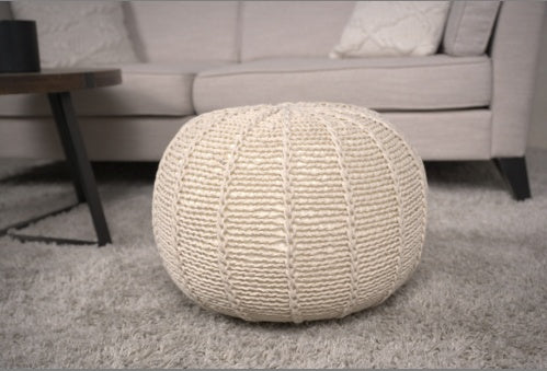 Cotton Pouf Ottoman in beige with knitted texture, placed in a modern living room as floor decor. Ideal as a footrest or extra seating.