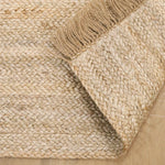 Hand-woven jute rug with fringe edges, adding a natural, rustic touch to living room or bedroom decor.