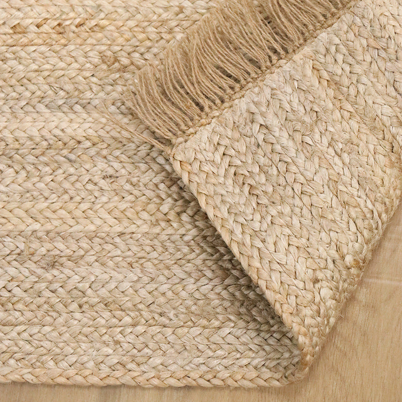 Hand-woven jute rug with fringe edges, adding a natural, rustic touch to living room or bedroom decor.