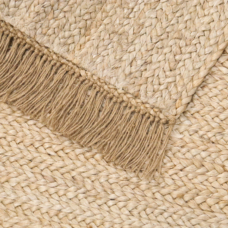 Hand-woven jute rug with fringe edges, adding a natural, rustic touch to living room or bedroom decor.