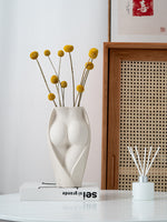 Contemporary ceramic vase with body-shaped design, holding yellow billy balls, placed on a white table for modern home aesthetics.