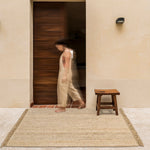 Hand-woven jute rug with fringe edges, adding a natural, rustic touch to living room or bedroom decor.