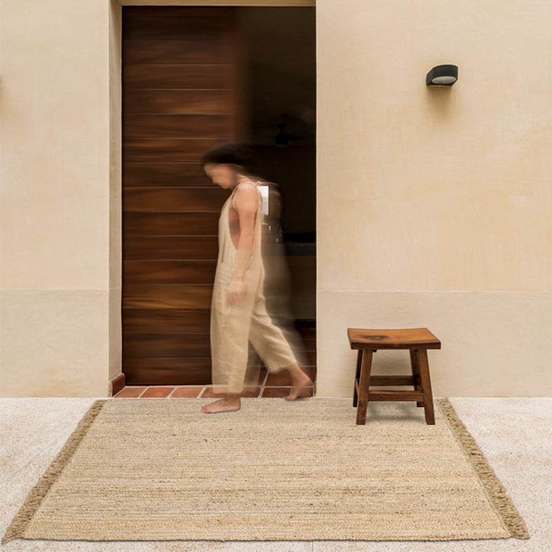 Hand-woven jute rug with fringe edges, adding a natural, rustic touch to living room or bedroom decor.