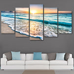 Ocean wall art in 5 panels showing sunset beach waves, mounted above a white sofa with blue pillows. Canvas design, no frame included.