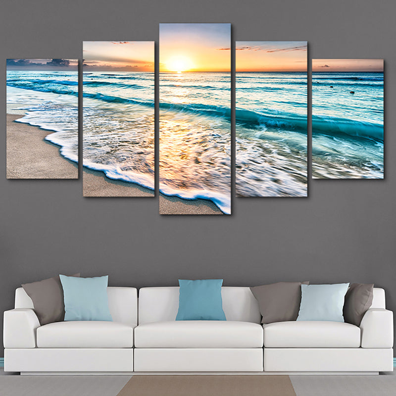 Ocean wall art in 5 panels showing sunset beach waves, mounted above a white sofa with blue pillows. Canvas design, no frame included.