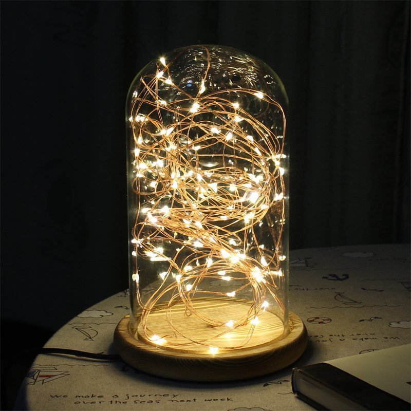 Atmosphere LED Night Lamp with dimming switch in a glass dome and wooden base, glowing warmly on a table. Ideal for cozy home decor.